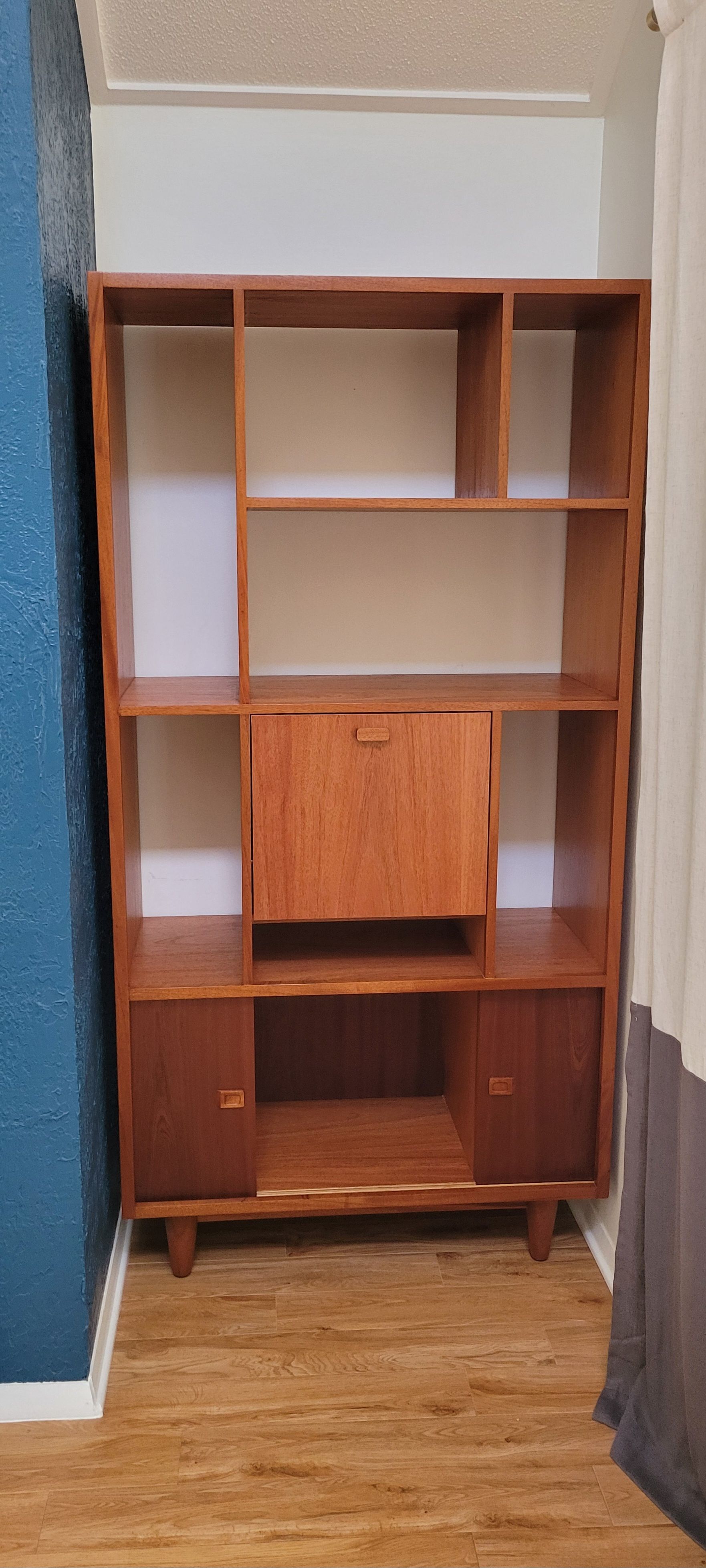 A wooden bookshelf is sitting in a room next to a blue wall.
