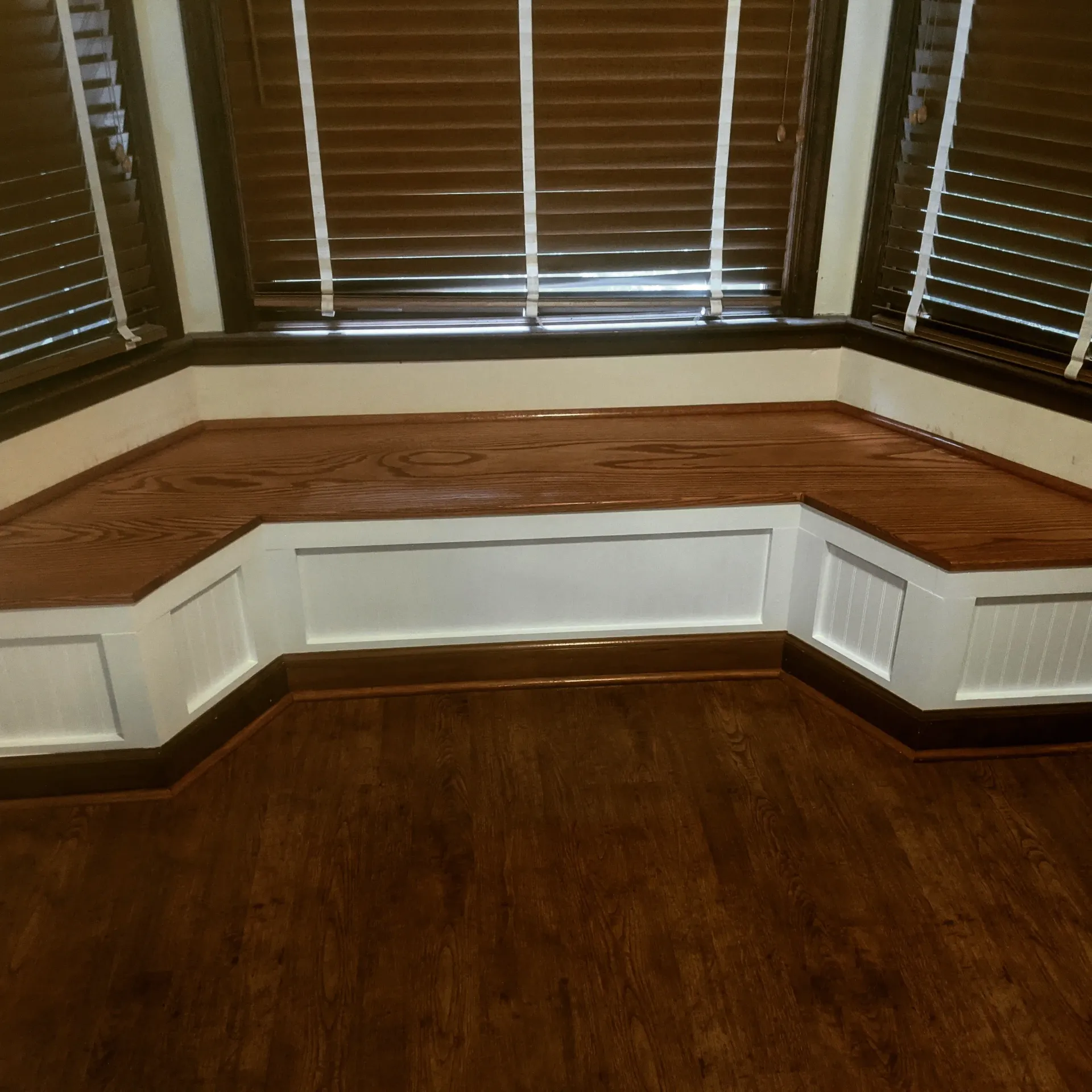 A wooden bench in front of a window with blinds.