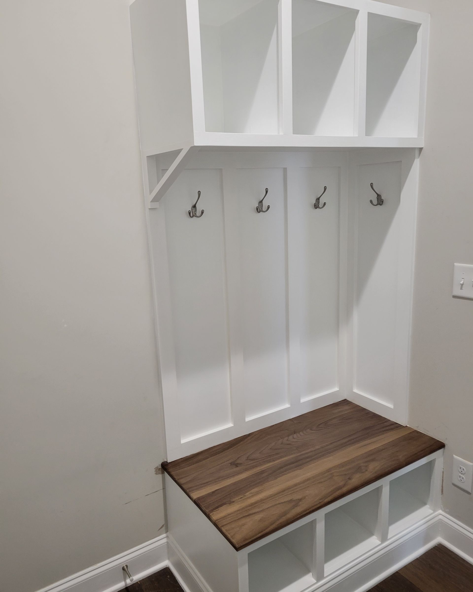 There is a bench in the corner of the room with hooks on the wall.