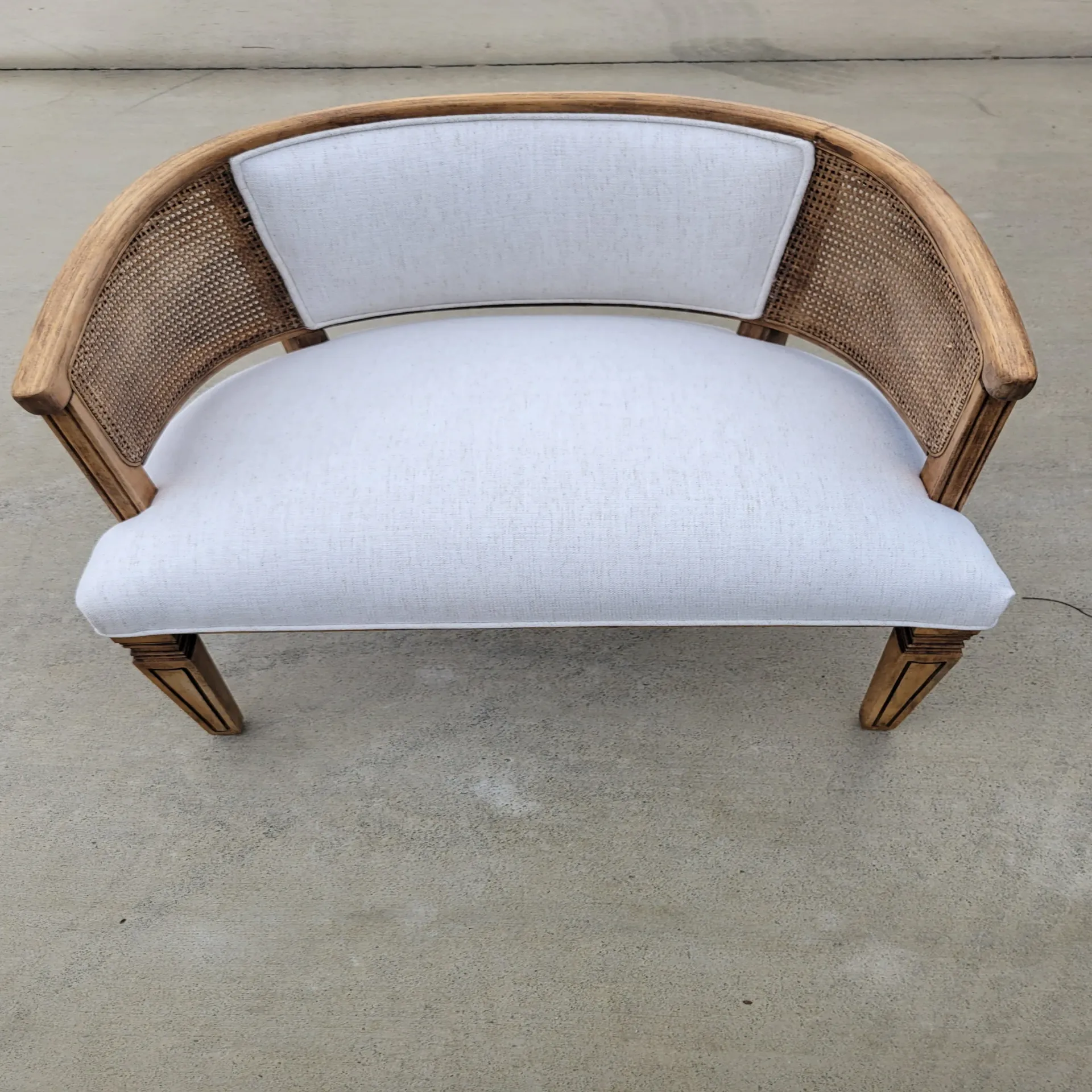 A wicker chair with a white cushion is sitting on a concrete surface.
