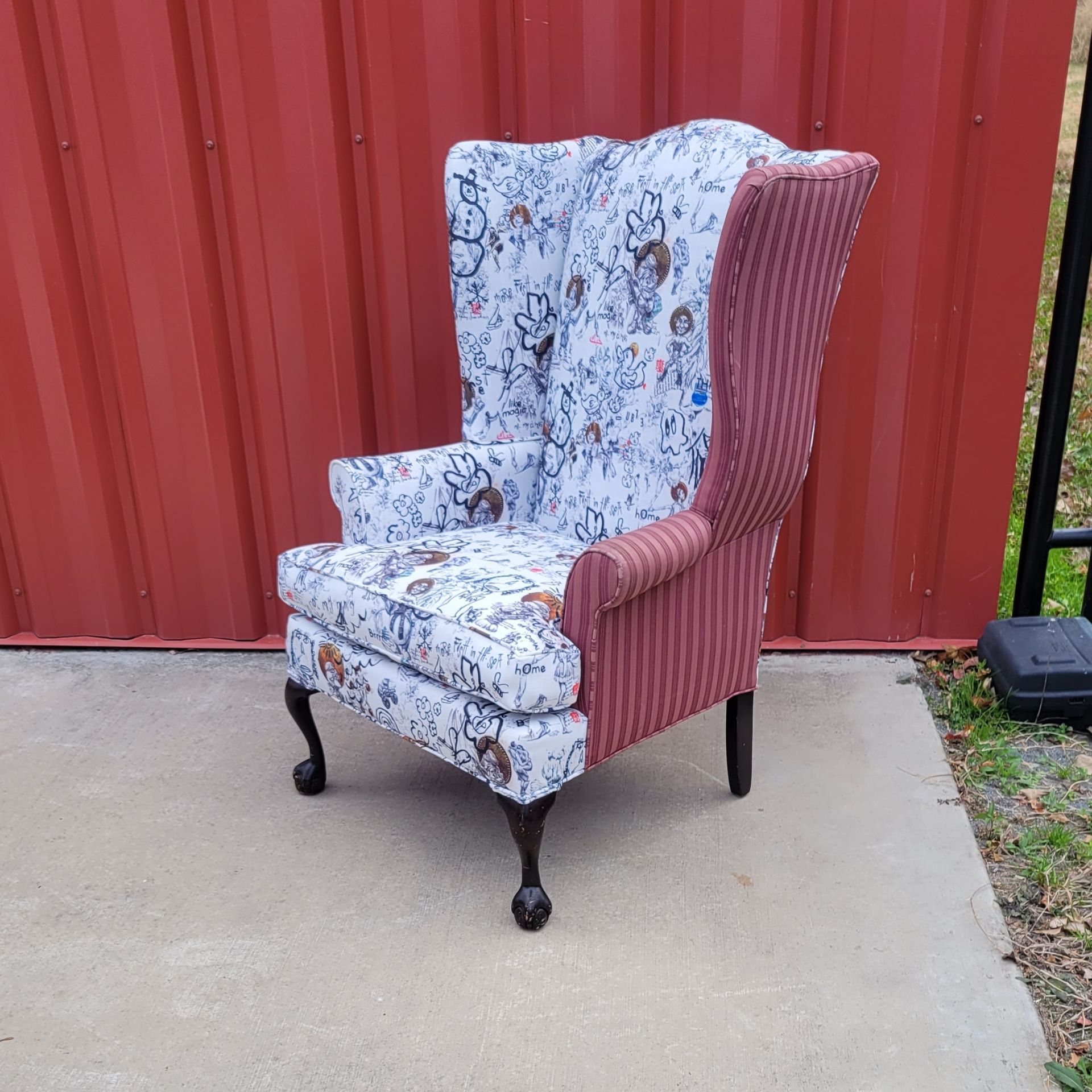 A chair is sitting on a sidewalk in front of a red wall.