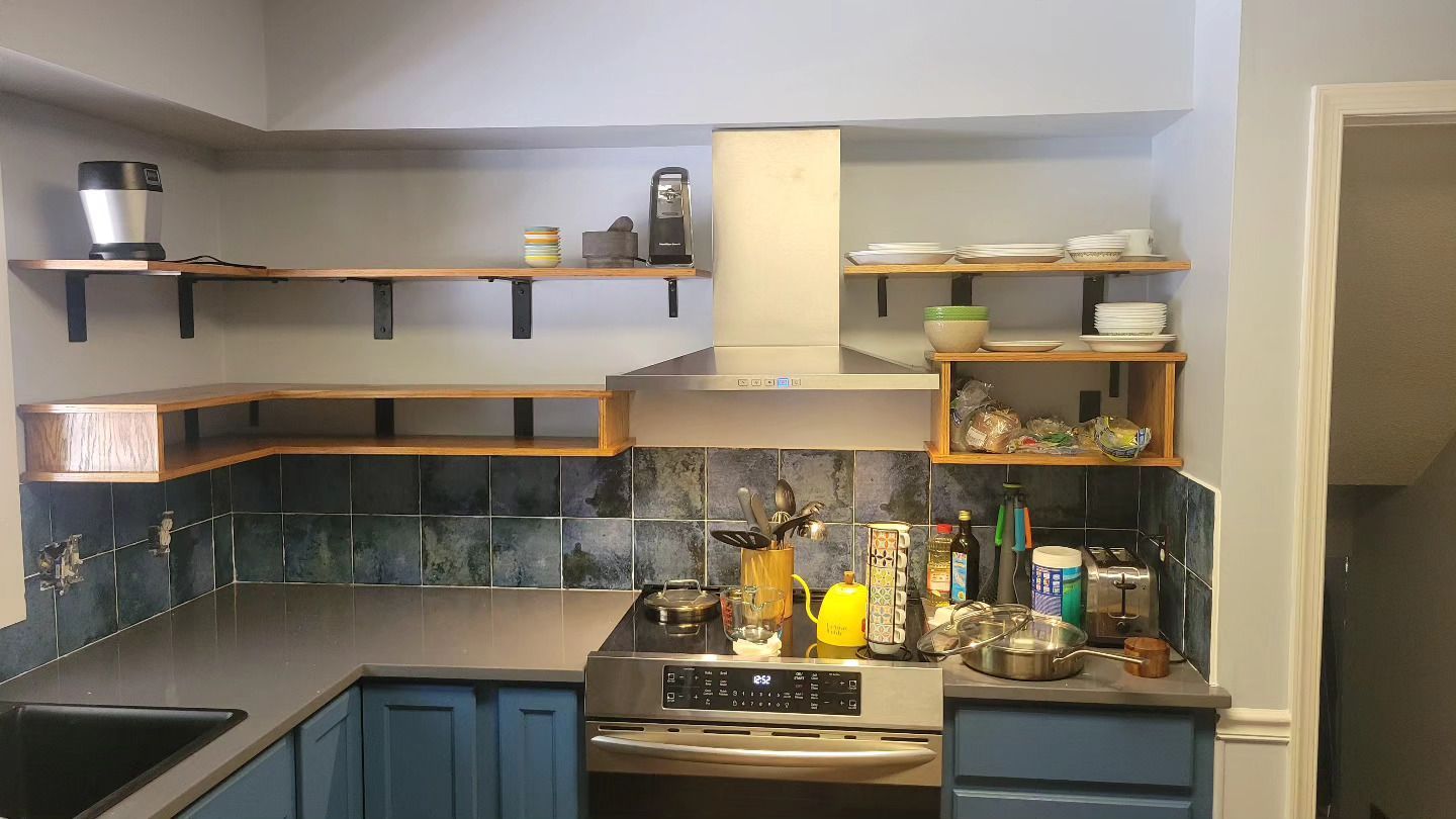 A kitchen with blue cabinets , a stove , a sink , and shelves.