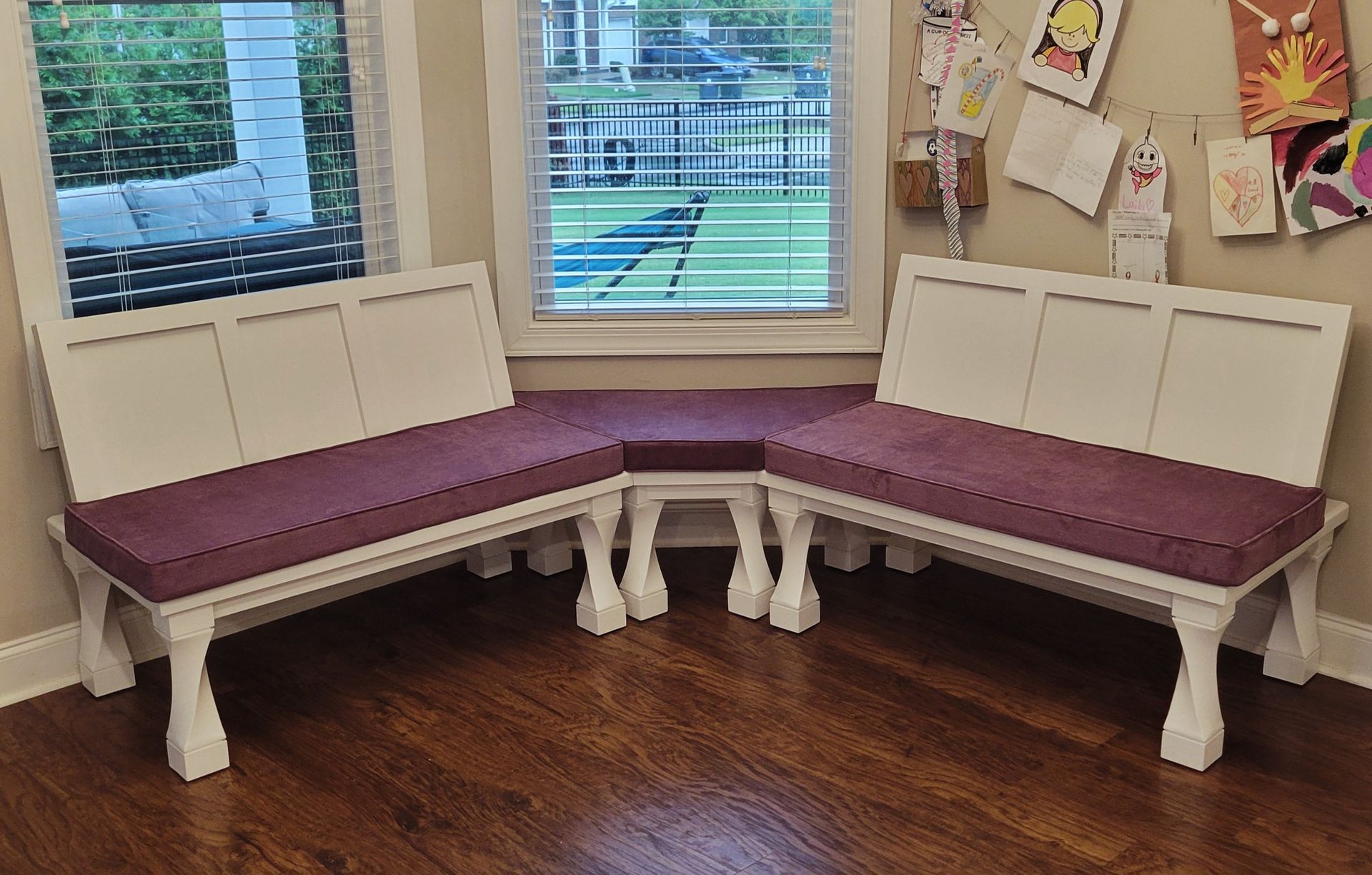 A corner bench with purple cushions in a living room next to a window.