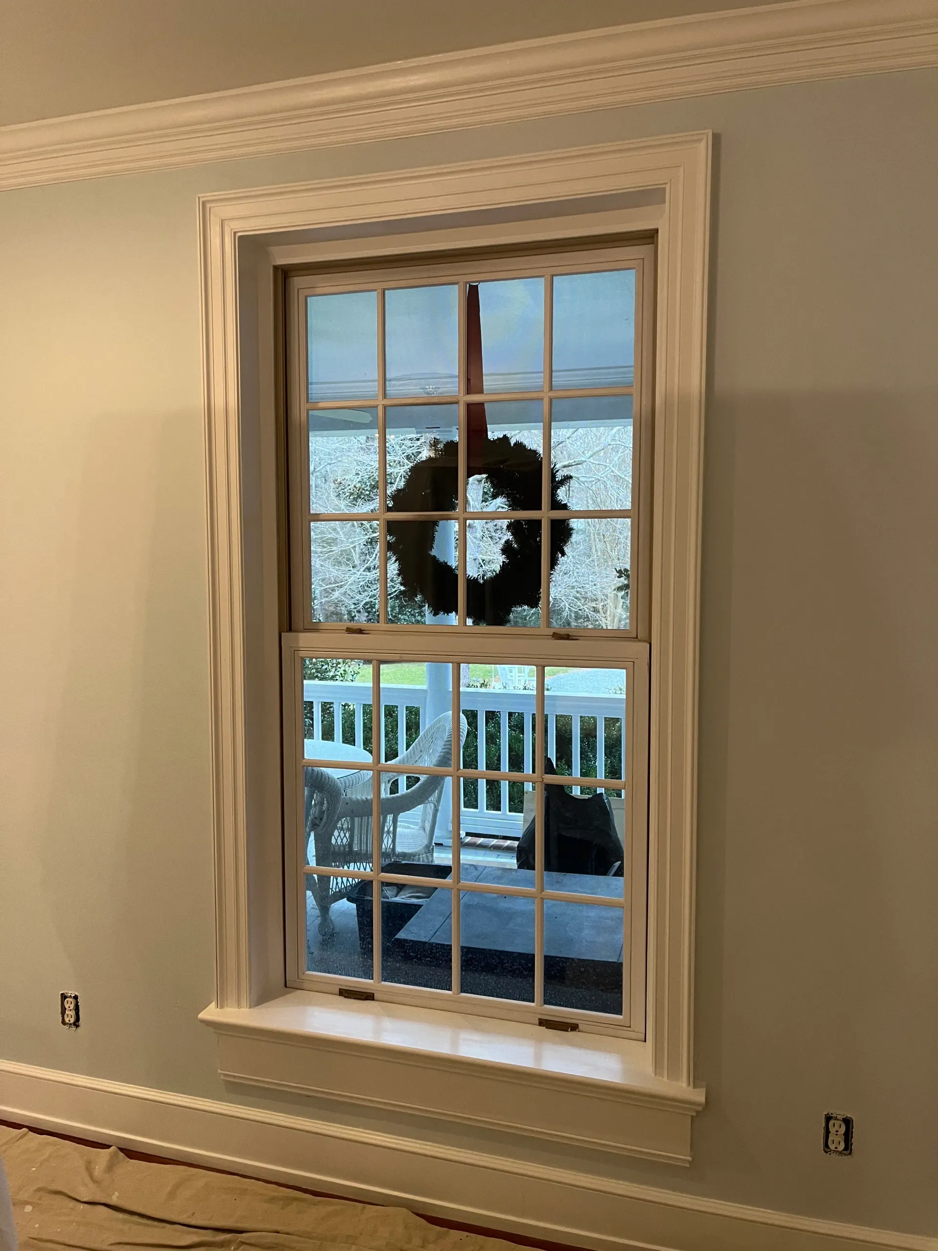 A window with a wreath hanging from it and a view of a porch.