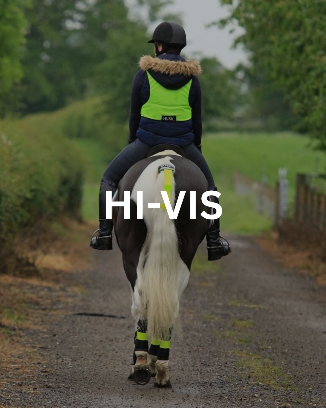 Person on horse wearing hi-vis vest and leg wraps on a dirt path, horse's tail also has hi-vis.