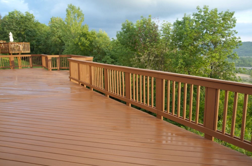 A large wooden deck with a fence and trees in the background