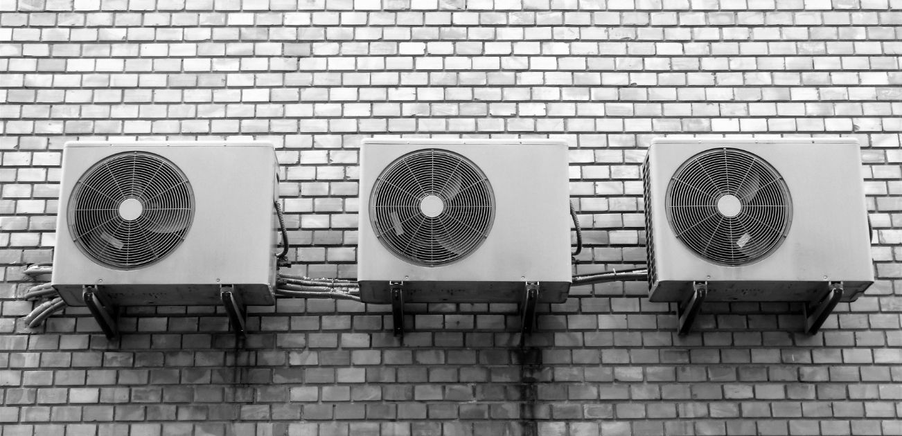 Three air conditioners are mounted on the side of a brick building.