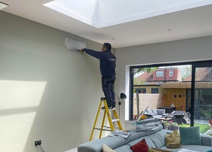 A man is standing on a ladder in a living room painting a wall.