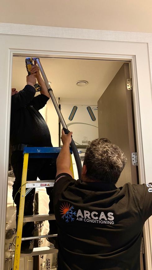 A man is standing on a ladder in a living room painting a wall.
