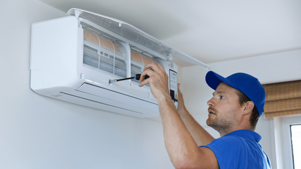 A man is fixing an air conditioner with a screwdriver.