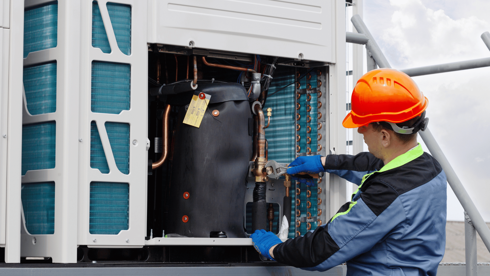 A man wearing a hard hat is working on an air conditioner.