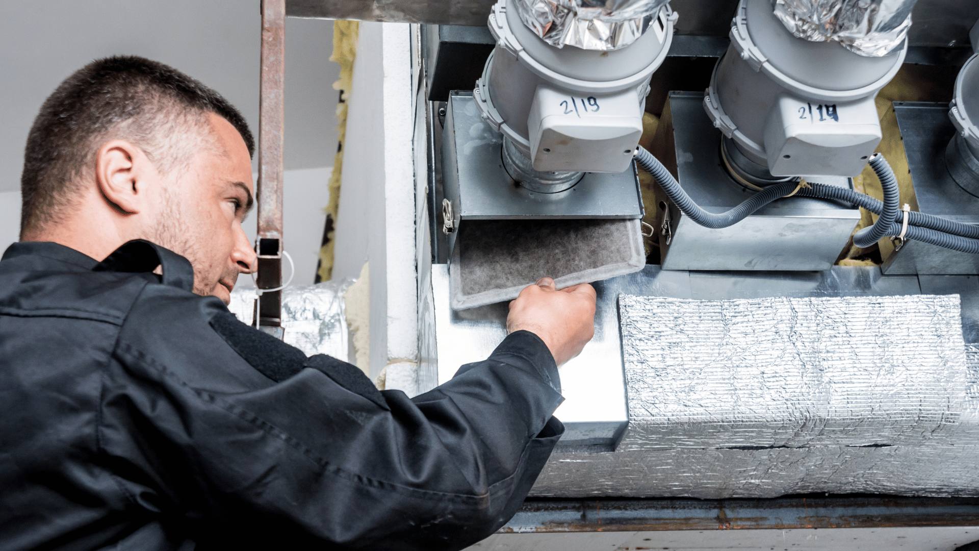 A man is working on a ventilation system in a building.