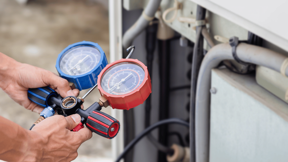 A person is holding two gauges in their hands while working on an air conditioner.