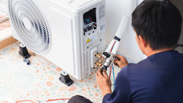 A man is sitting on the floor fixing an air conditioner.