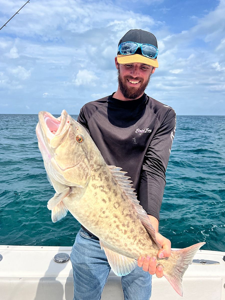 A man is holding a large grouper on a boat in the ocean.