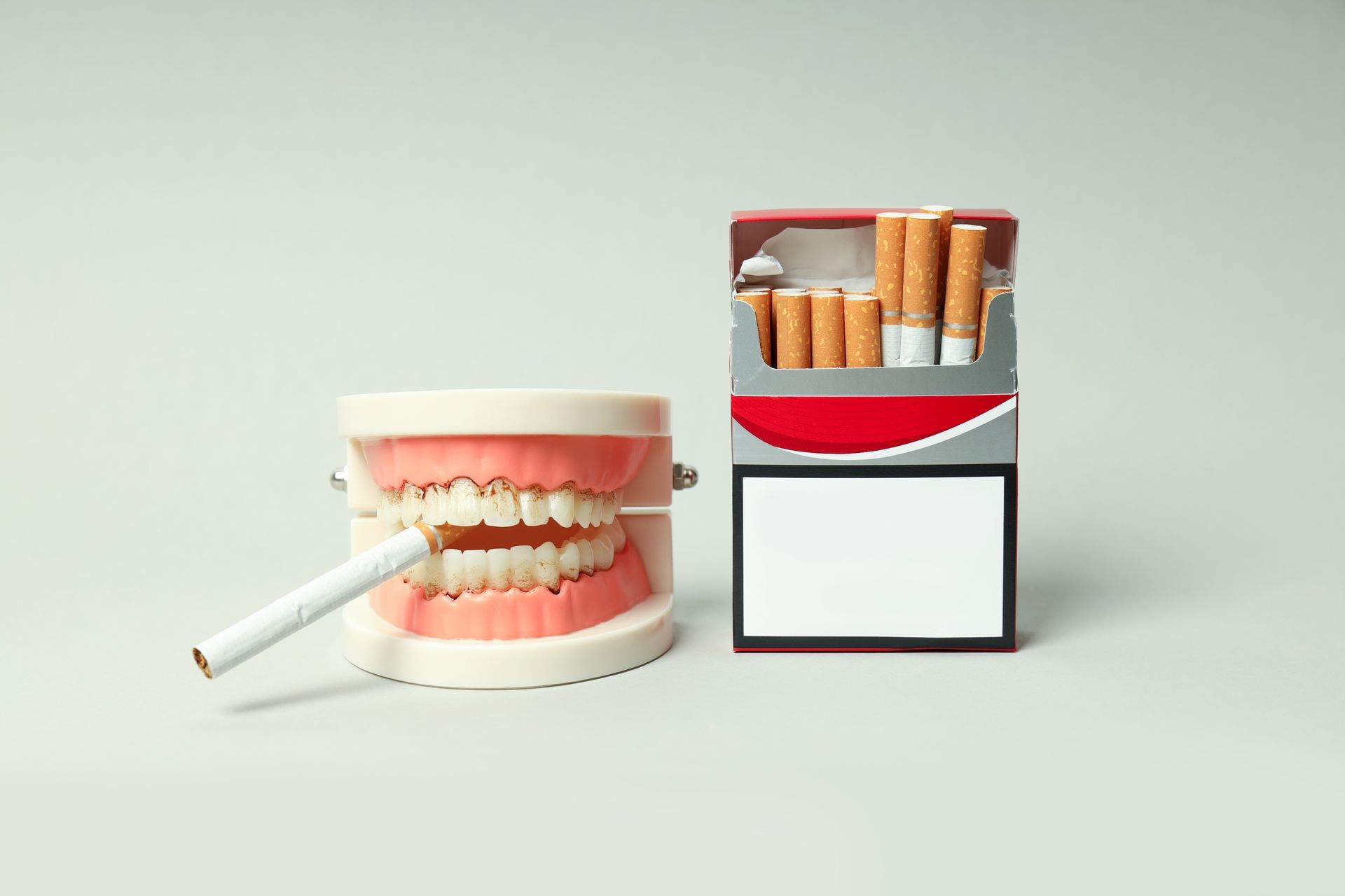 unlit cigarette in dentures sitting next to a pack of cigarettes 