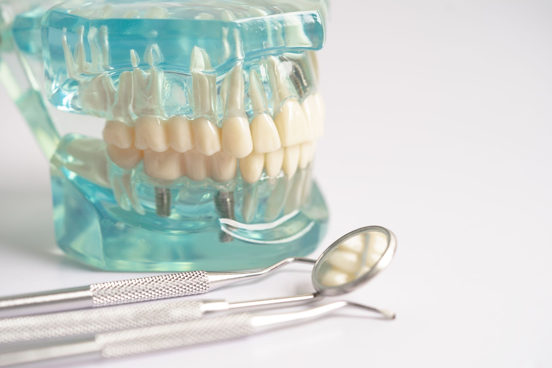 Dental model with tools, including mirror and probes, on white surface.