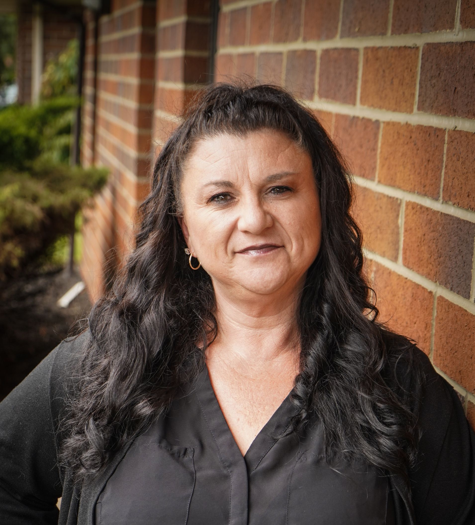 A woman with long dark hair is standing in front of a brick wall.