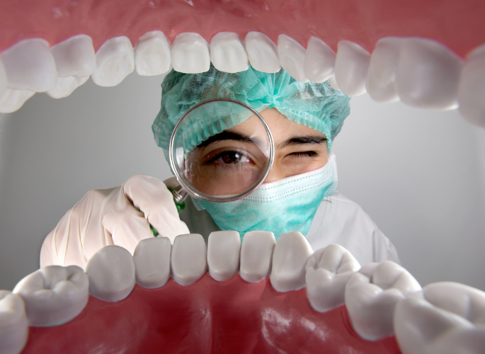 A dentist is looking through a magnifying glass at a model of teeth.