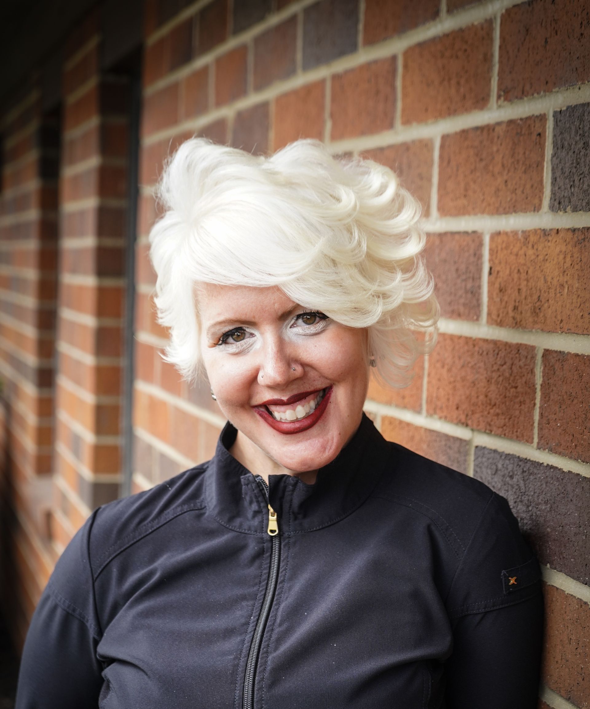 A woman with blonde hair is smiling in front of a brick wall.