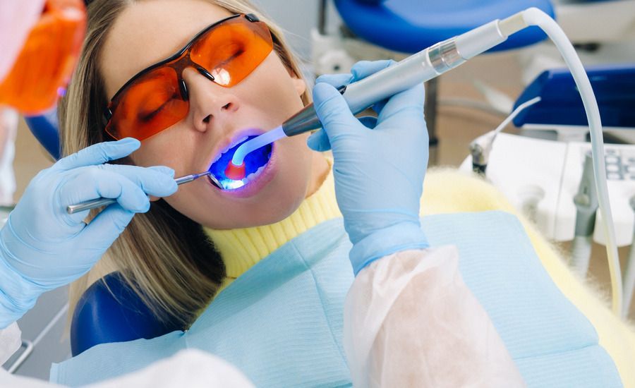 A woman is getting her teeth whitened by a dentist.