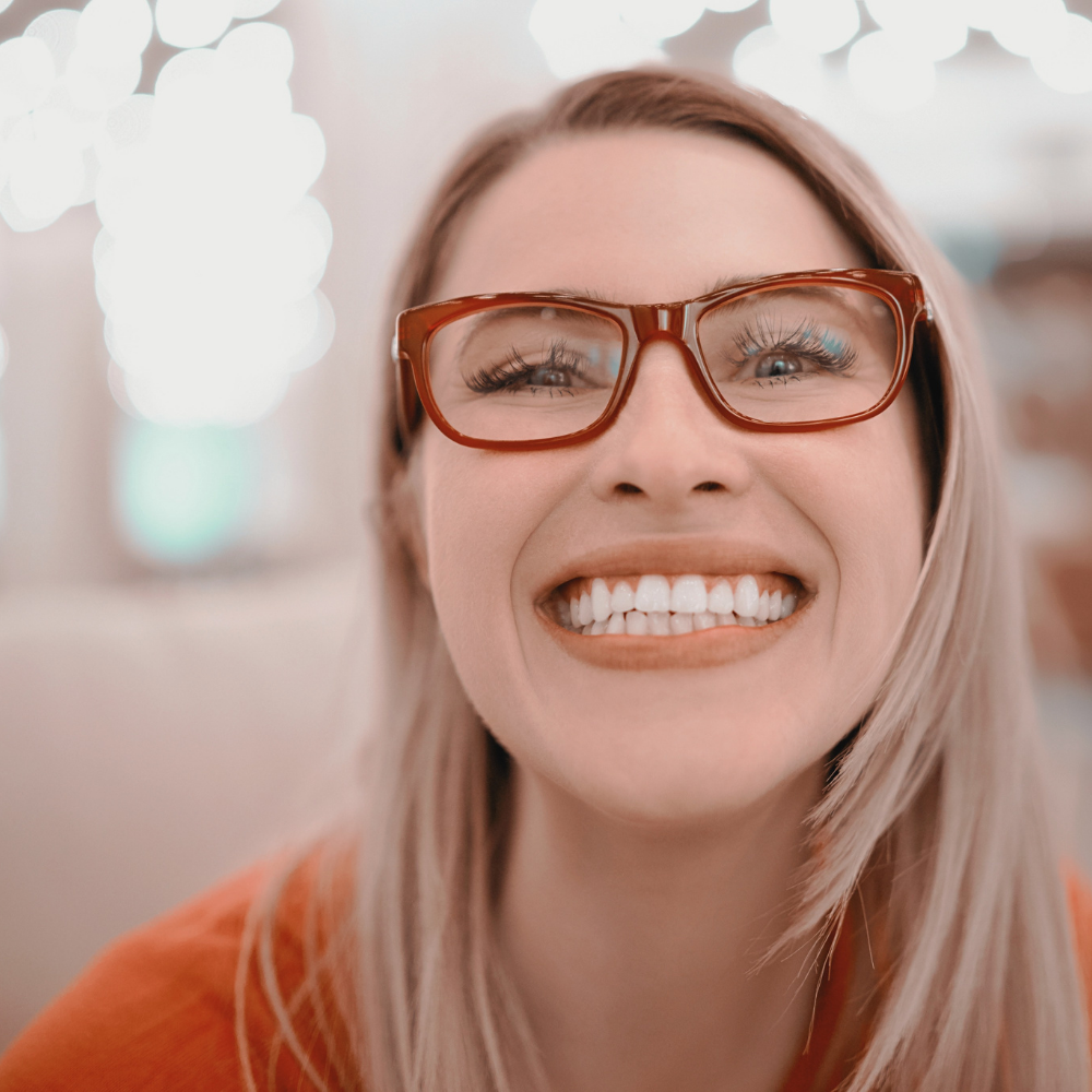 A woman wearing glasses is smiling and looking at the camera