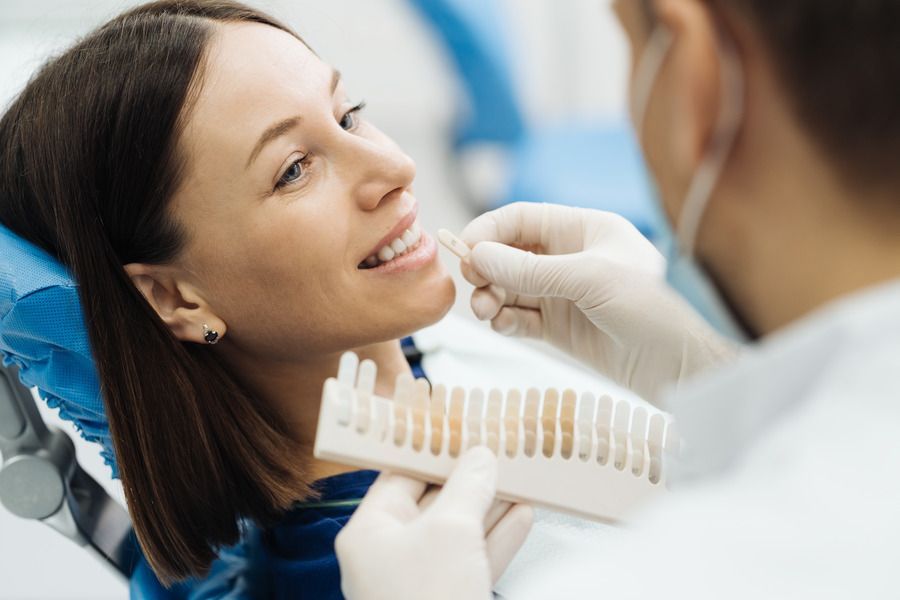 A woman is sitting in a dental chair while a dentist examines her teeth.