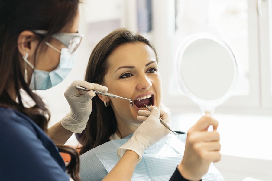 A woman is getting her teeth examined by a dentist while looking in a mirror.