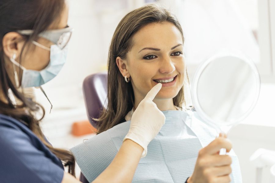 A woman is sitting in a dental chair looking at her teeth in a mirror.