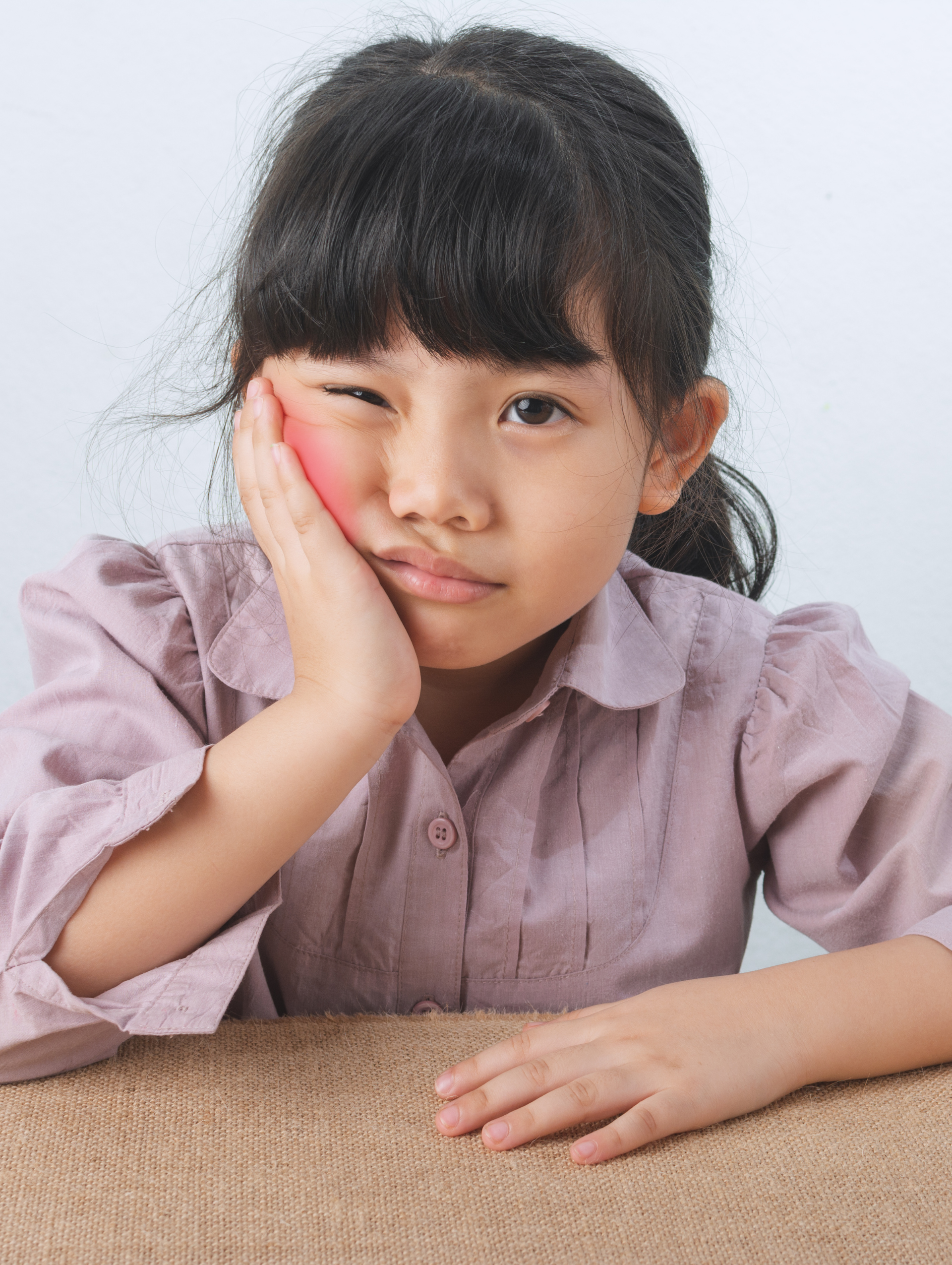 A little girl is sitting at a table with her hand on her face.