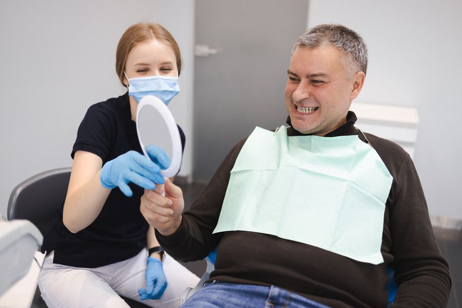 A man is sitting in a dental chair looking at his teeth in a mirror.