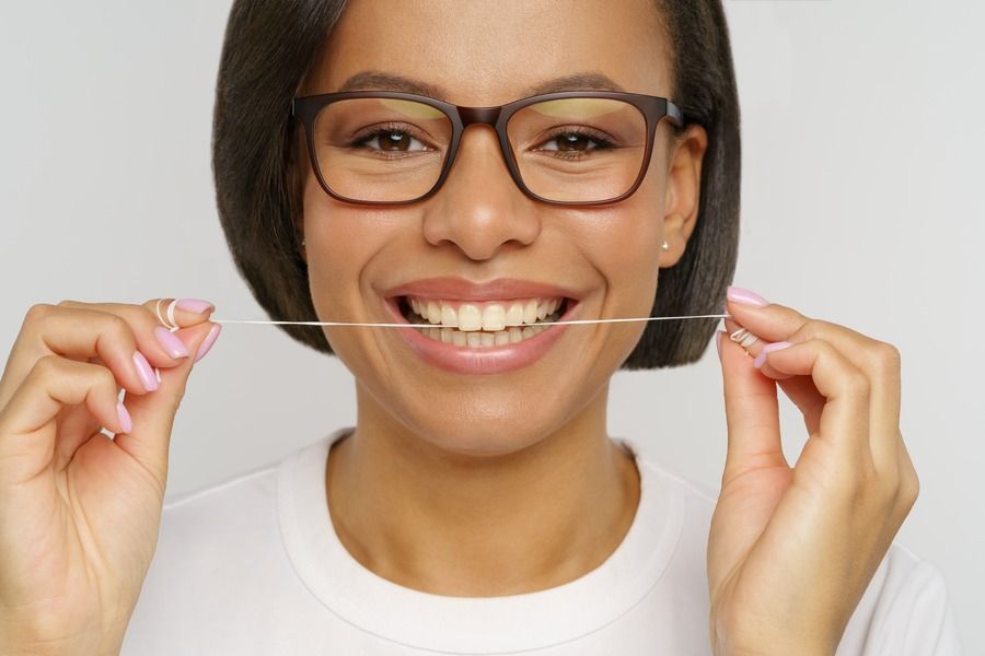 A woman wearing glasses is flossing her teeth with a dental floss.