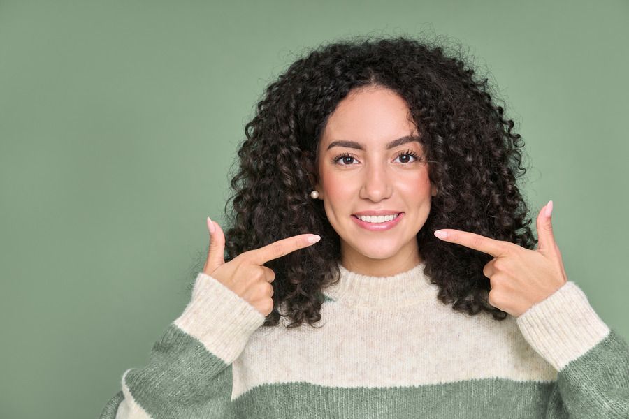 A woman with curly hair is pointing at her teeth.