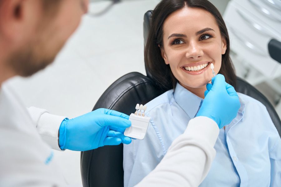 A woman is sitting in a dental chair while a dentist examines her teeth.