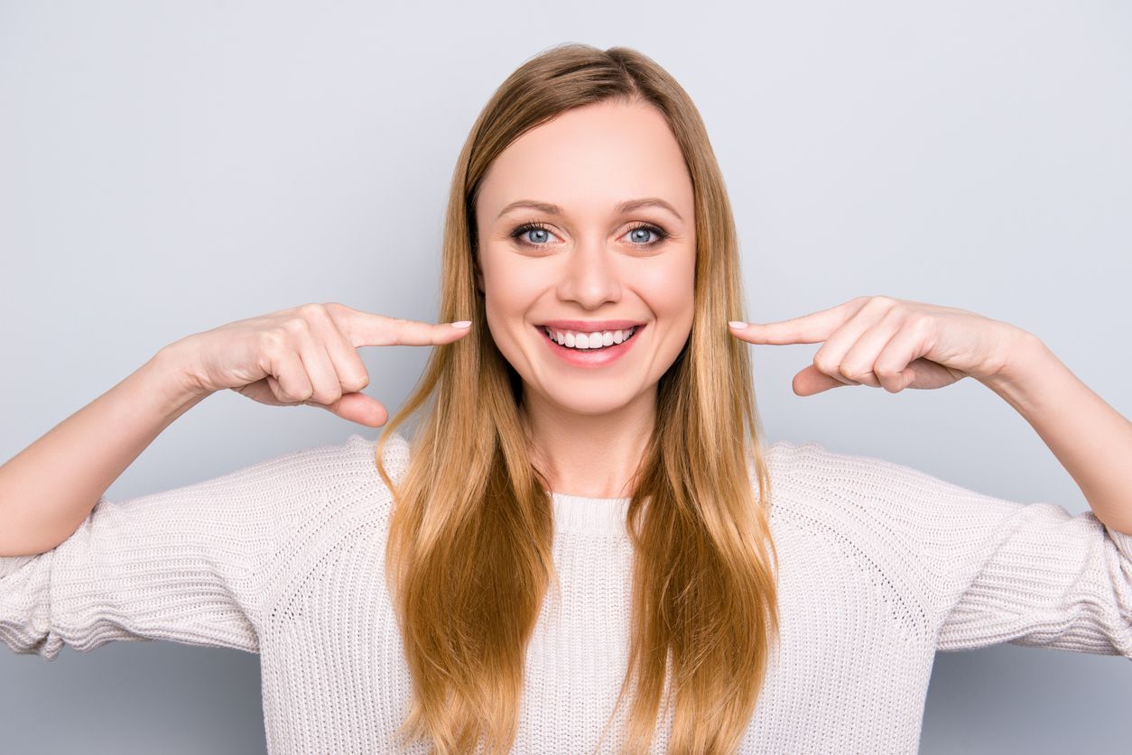 A woman is pointing at her teeth and smiling.