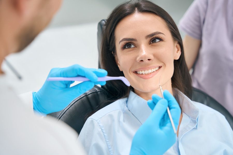 A woman is sitting in a dental chair while a dentist examines her teeth.