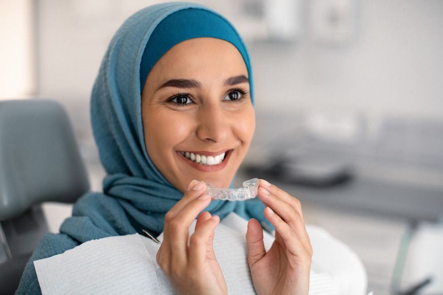 A woman in a hijab is sitting in a dental chair holding a clear brace.