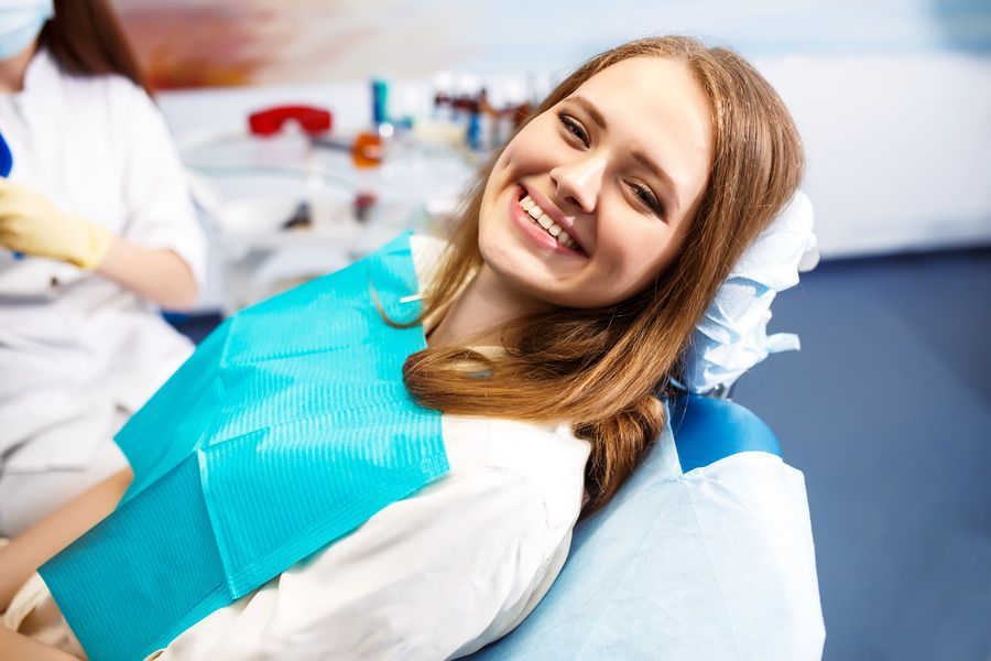 A woman is smiling while sitting in a dental chair.