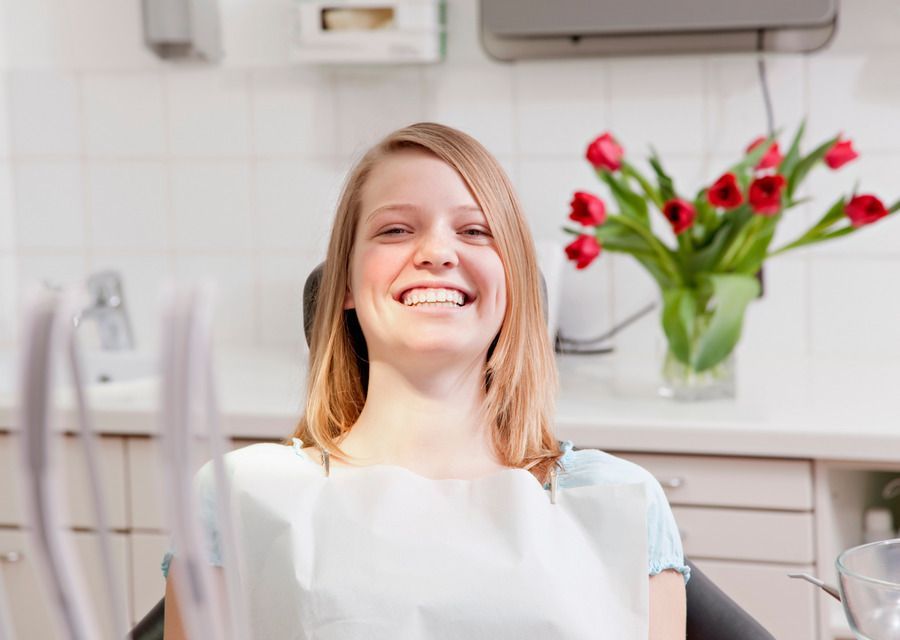 A woman is smiling while sitting in a dental chair.