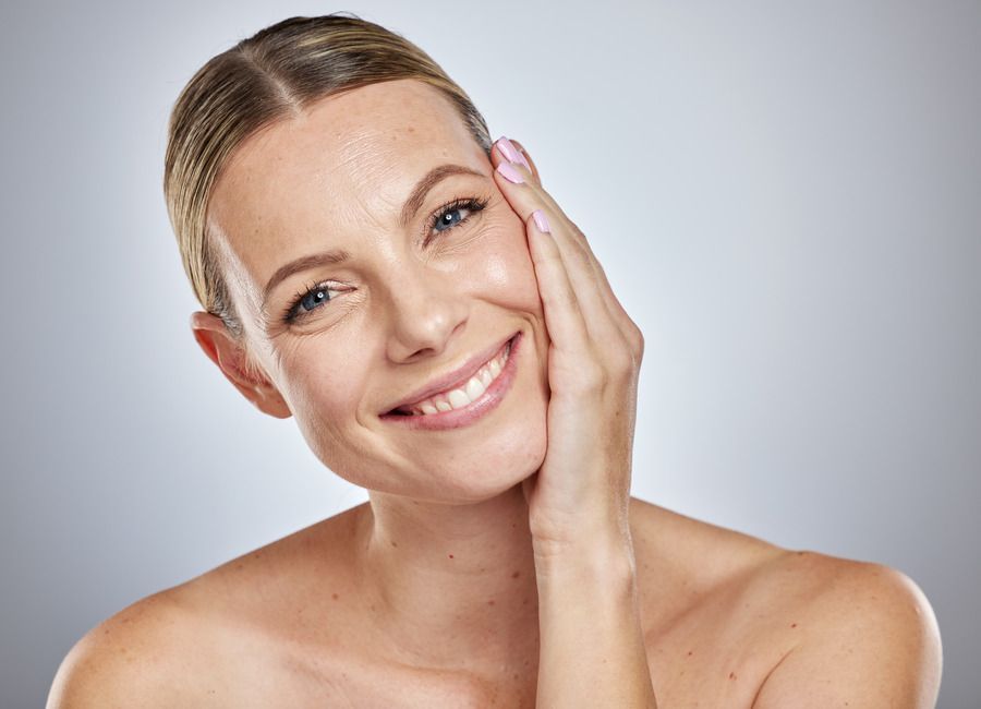 A woman is smiling and touching her face with her hand.