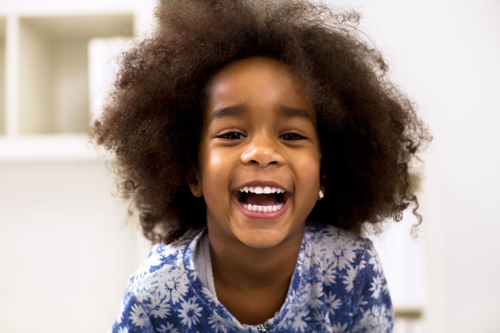 Smiling child with curly hair wearing a blue floral shirt.