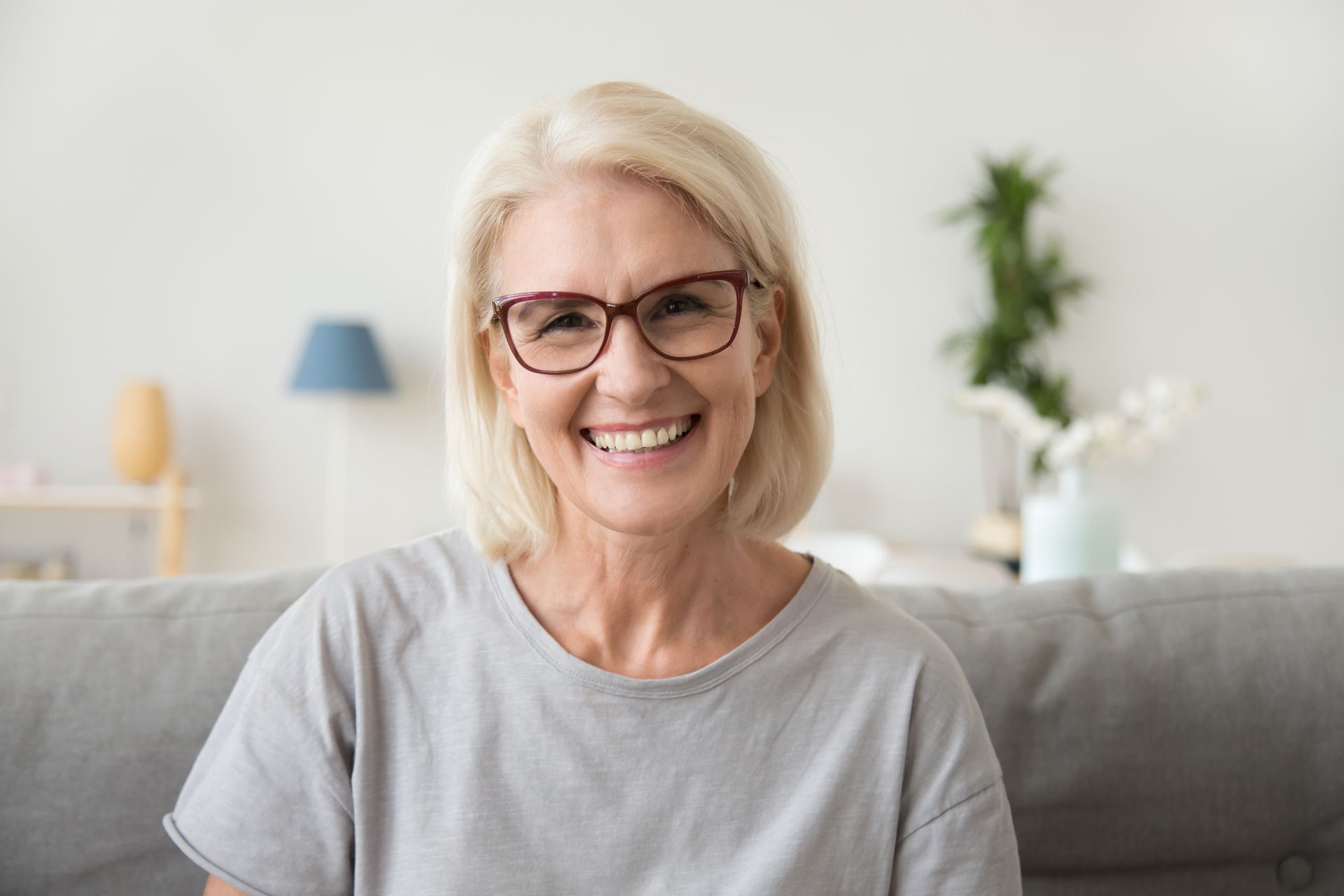 Woman with glasses smiles; sitting indoors on a couch. Woman with glasses smiles; sitting indoors on a couch.
