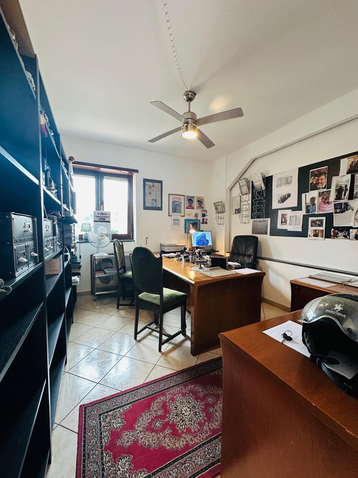 Una stanza con una scrivania, sedie, scaffali e un ventilatore a soffitto.