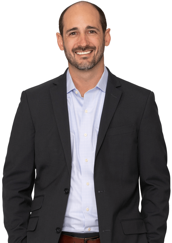 Man in a suit smiles, arms at his sides. He has short brown hair and a beard, with a light blue shirt under the suit.