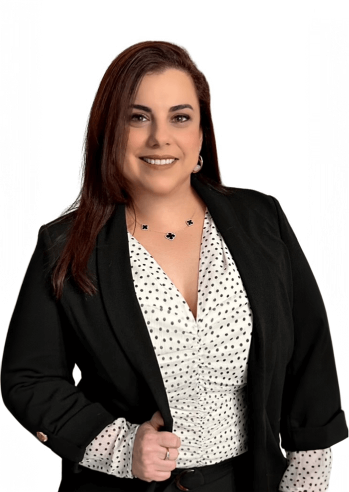 Woman in black blazer smiles, posing in front of white background, wearing polka dot blouse and jewelry.