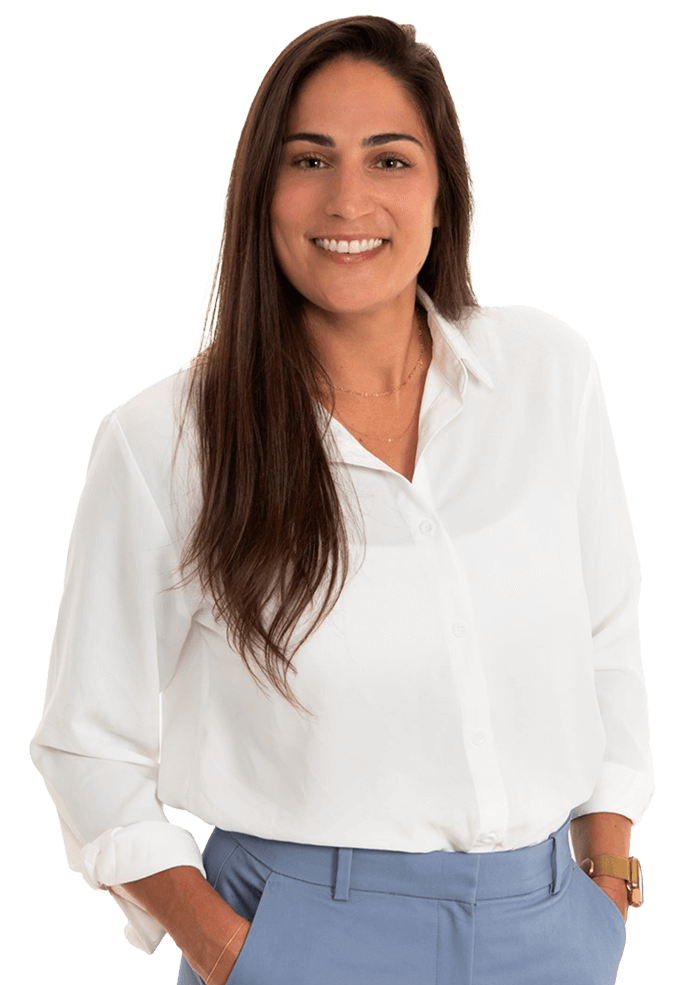Woman in white shirt and blue pants smiles, hands in pockets.