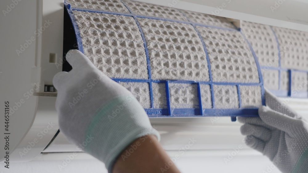 A person wearing white gloves is cleaning an air conditioner filter.