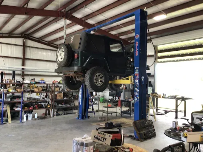 Jeep Wrangler on a blue car lift inside a workshop. Tools and equipment surround it.