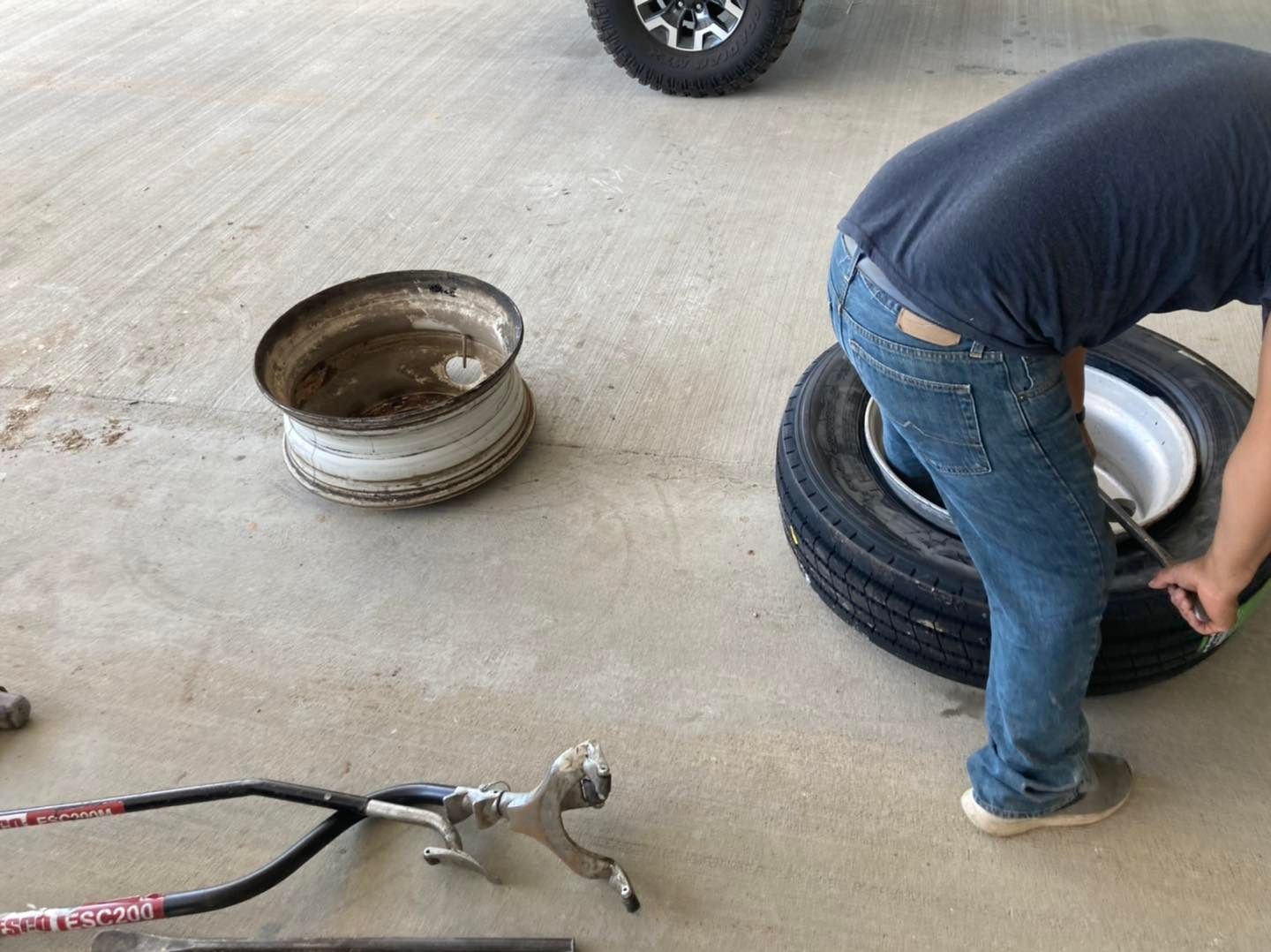 Man changing a tire, holding a tool. Old tire rim and tire on the ground, in a garage.