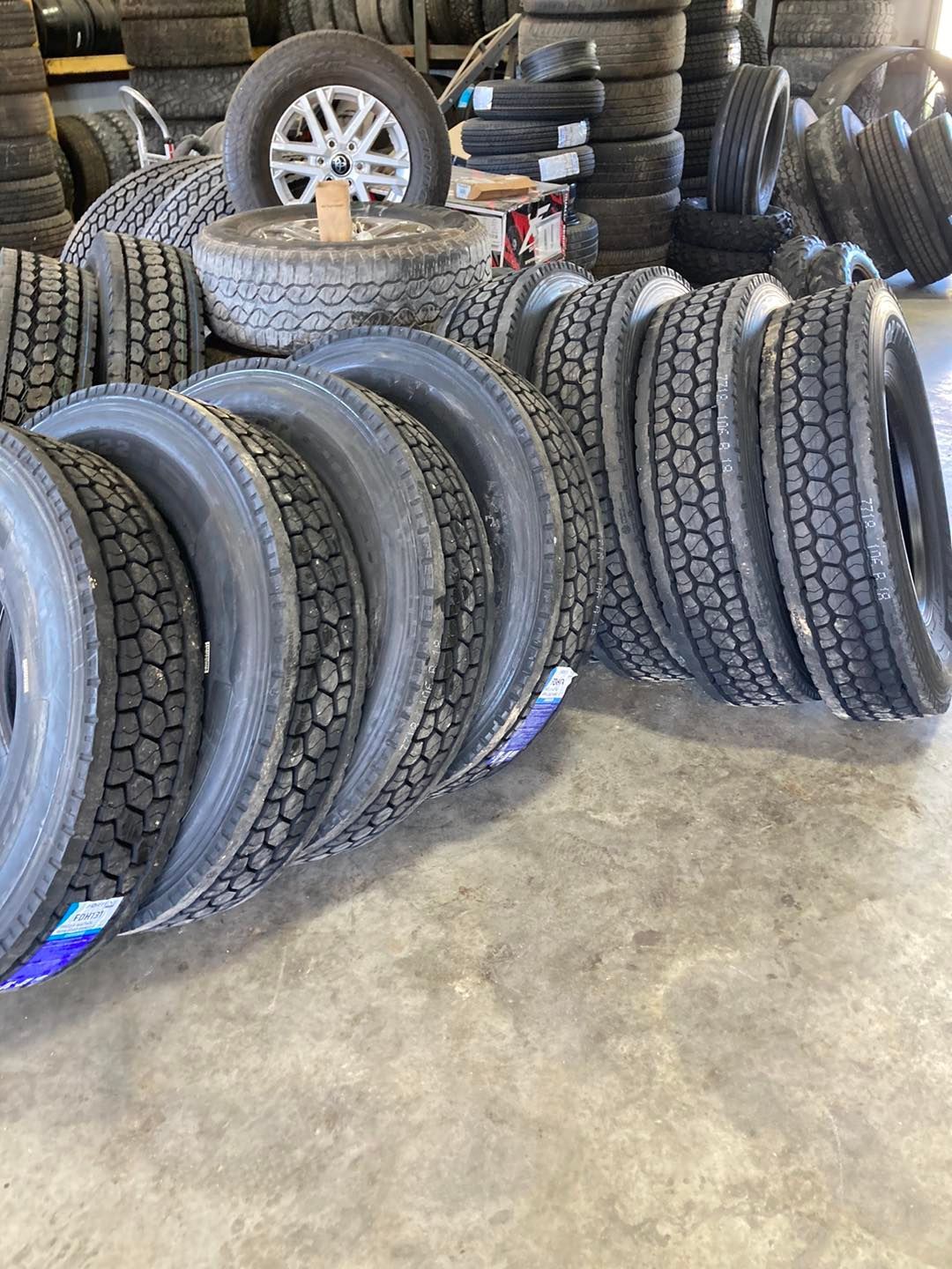 Tires stacked for sale at a tire shop. Dark rubber, visible tread. Gray floor in the foreground.